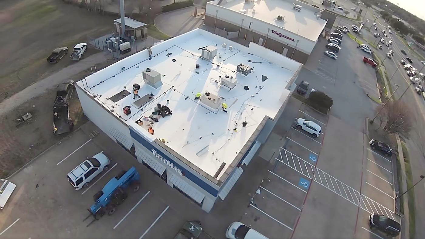 Drone view of a flat white commercial roof beside a parking lot