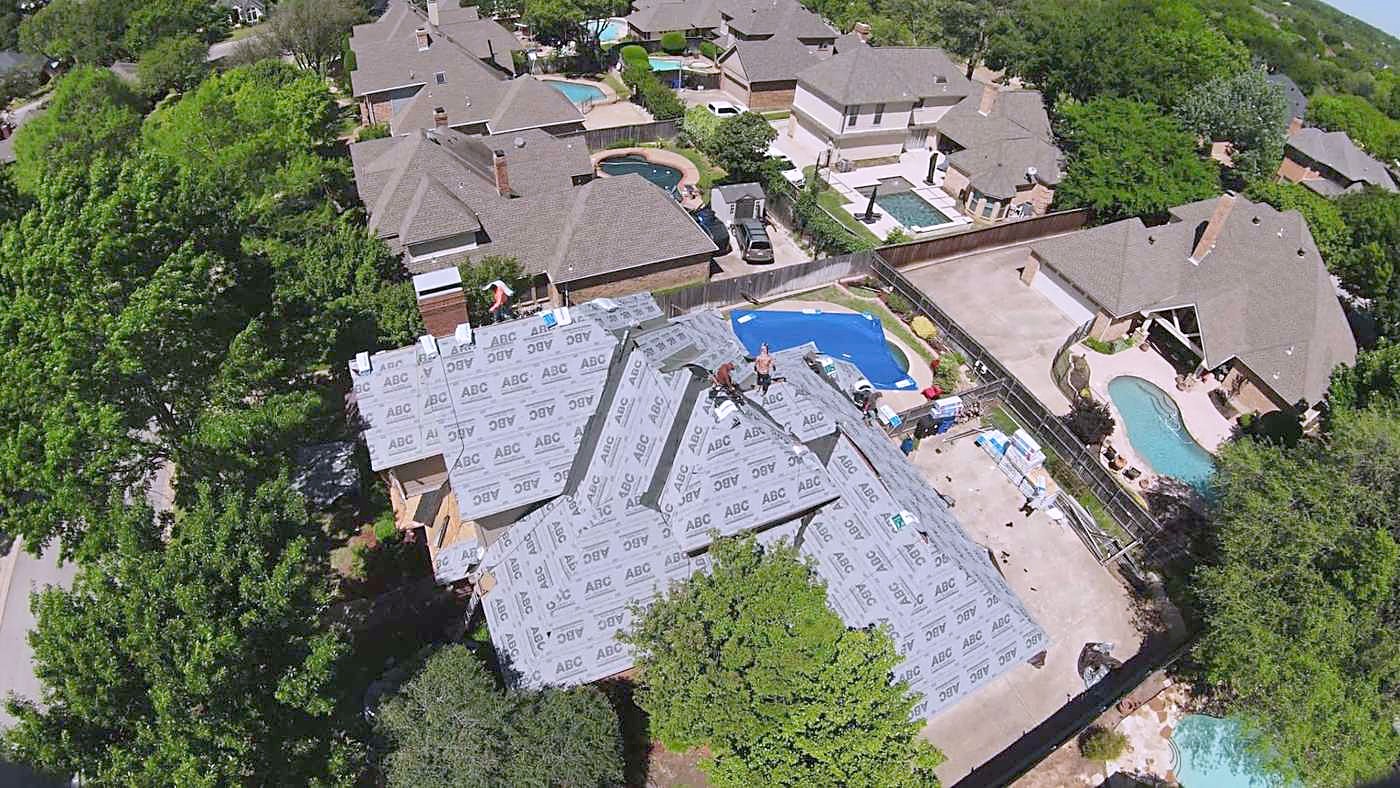 Aerial view of a large home mid-reroof, underlayment down beside the pool