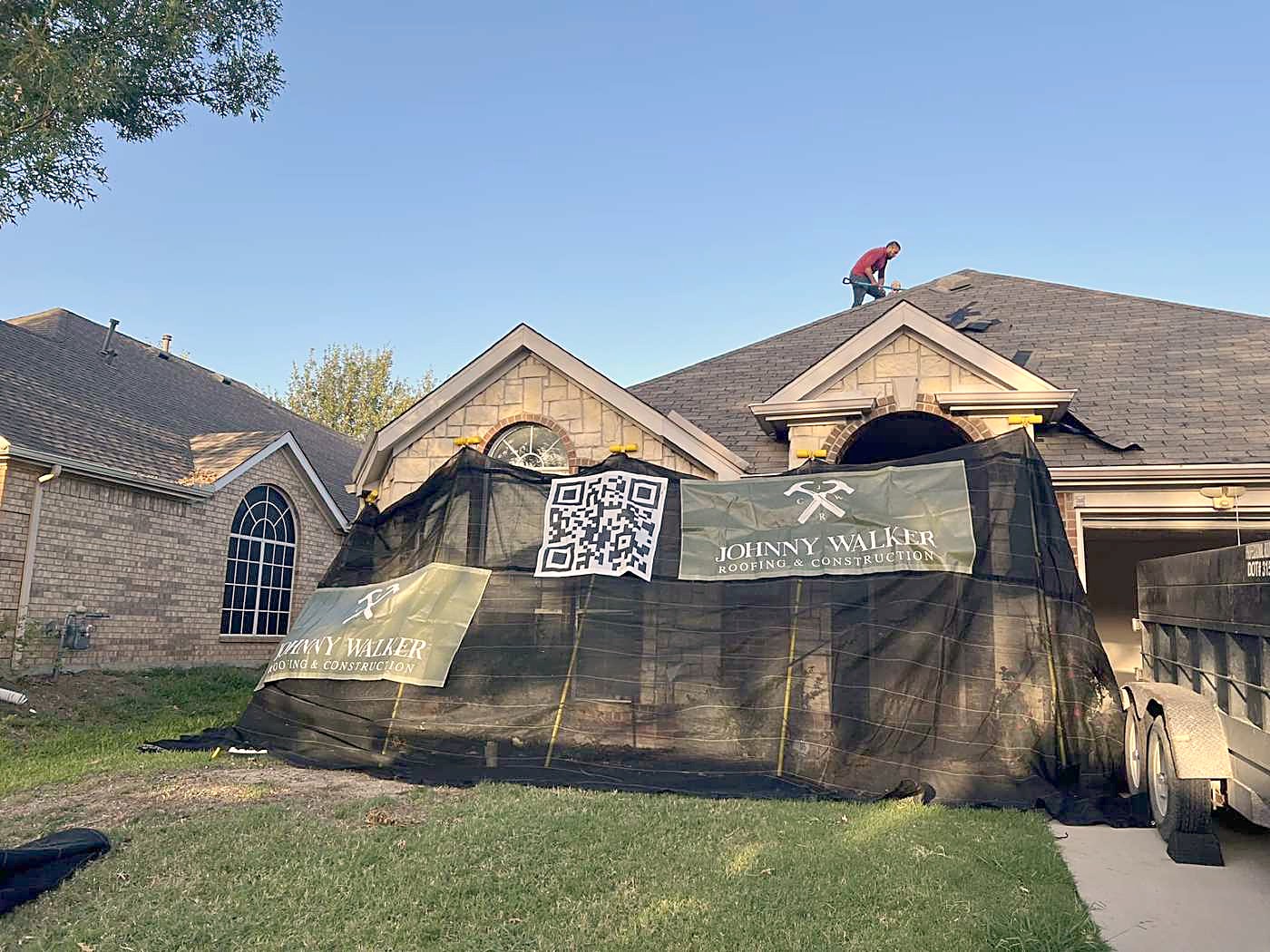 A home netted for a tear-off, with a Johnny Walker Roofing banner on the lawn