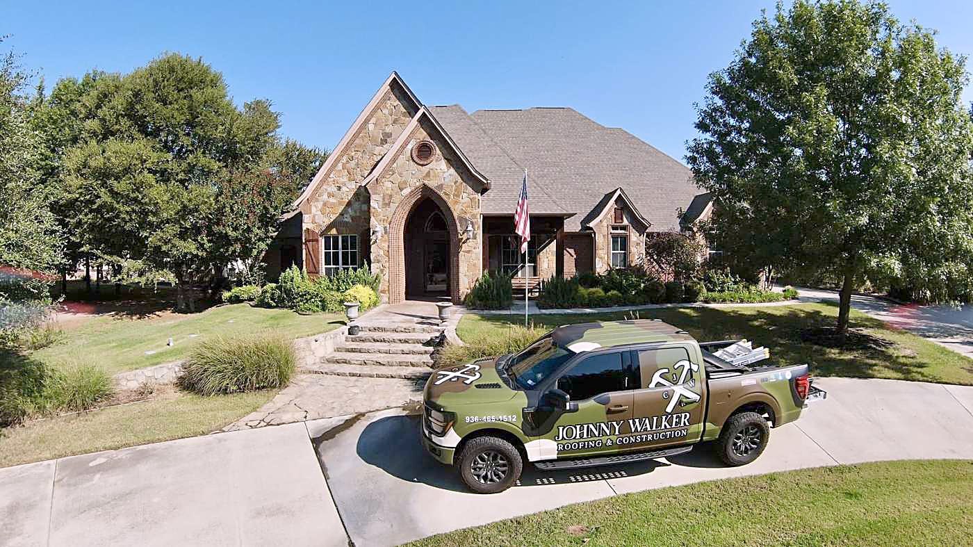 A wrapped Johnny Walker Roofing truck parked outside a stone home
